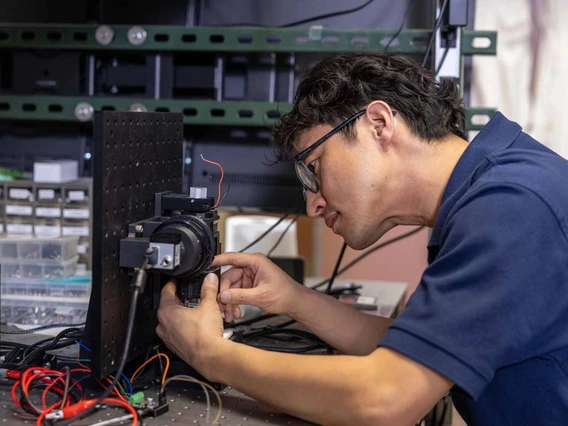 A man in blue shirt looks a microscope. 