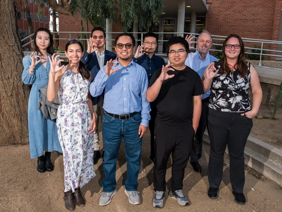 Eight people pose for a photo with hands raised to signify U of A college sign.