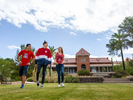 Three students in red shirts walk on a green lawn.