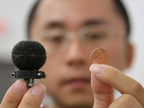 A man holds up a small 3D-printed black sphere in one hand, a penny in the other. The sphere is only about 3 times the size of the penny.