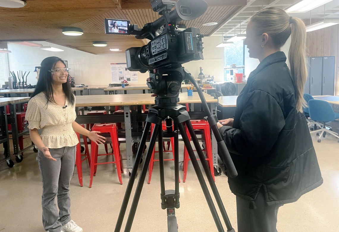 A student speaks to a reporter with a camera on a tripod