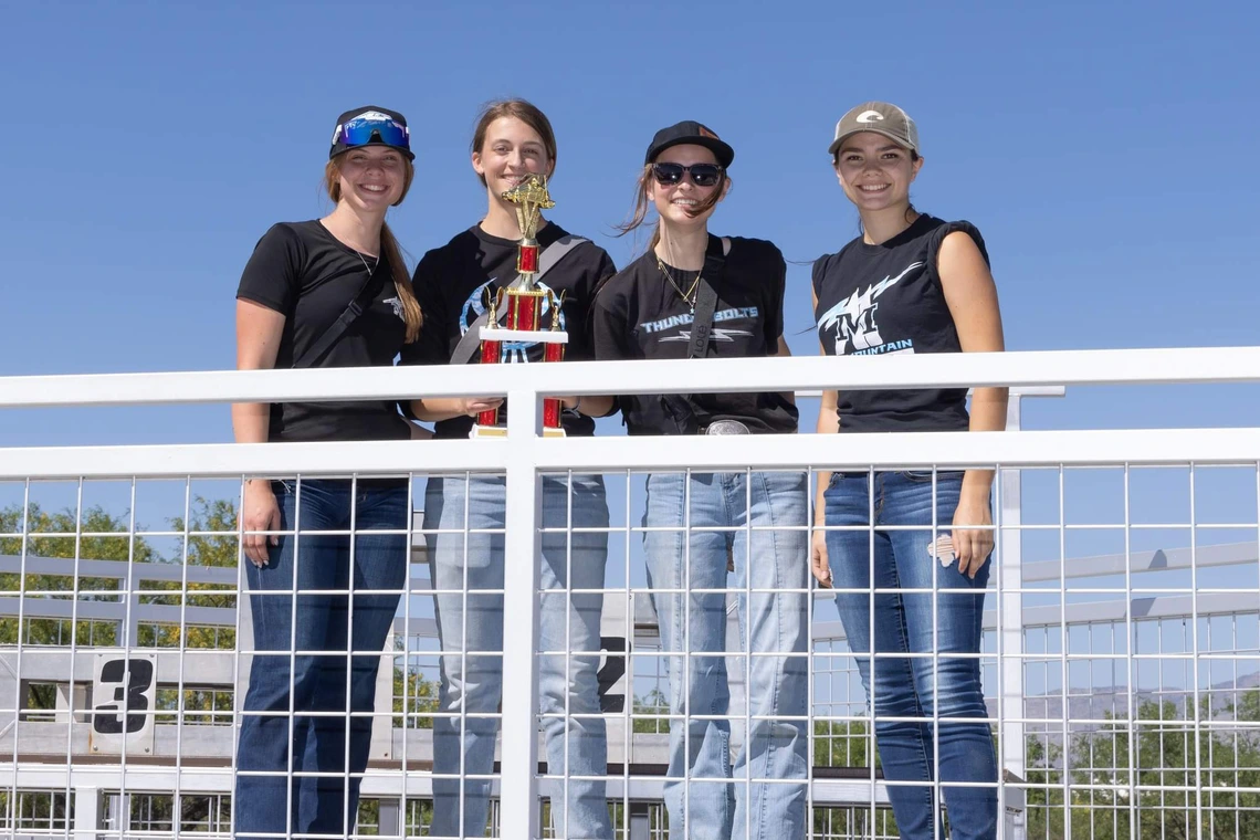 Four high school students pose outdoors with a trophy.