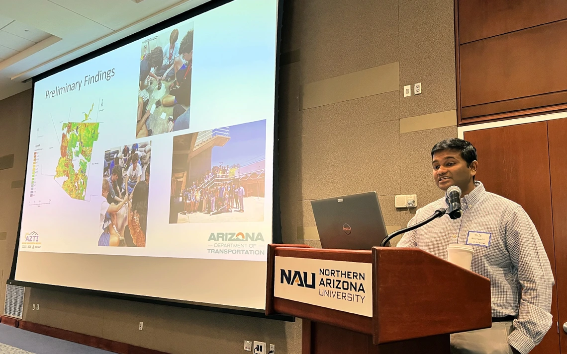 A man with brown hair stands in front of a presentation screen.