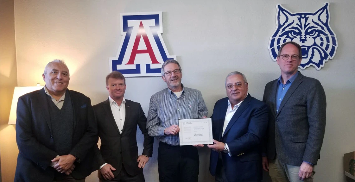 Five men stand in front of a wall with a University of Arizona block A and wildcat logo on it.
