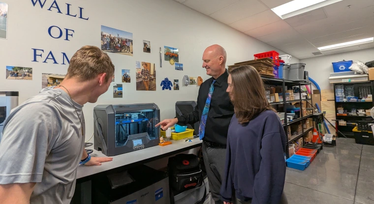 Three people surround a piece of equipment in a classroom