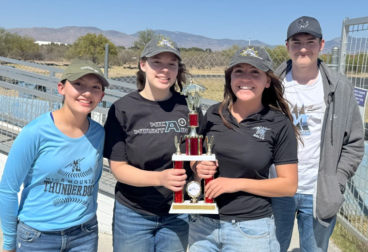 Four students pose outdoors with a trophy,