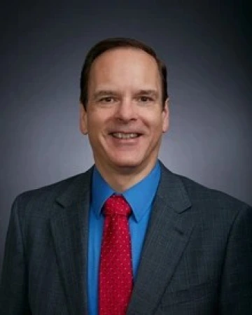 I man in a black suit and a light blue shirt poses for a photo.