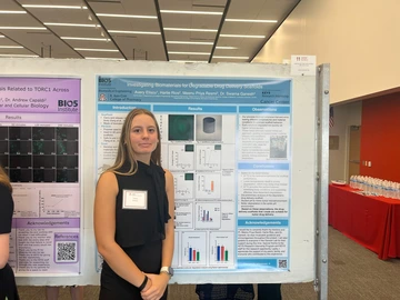 A woman in a black dress stands next to a poster.