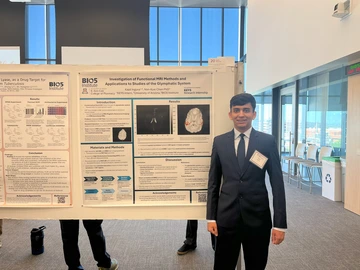 A man with brown hair stands next to a poster.