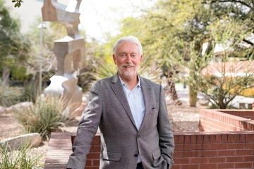A man with light hair poses for a photo in a grey suit.