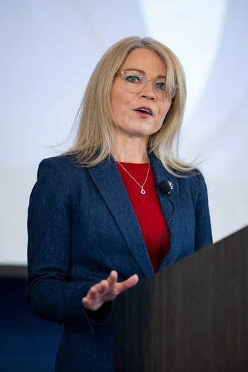A woman with blond hair speaks on a podium.